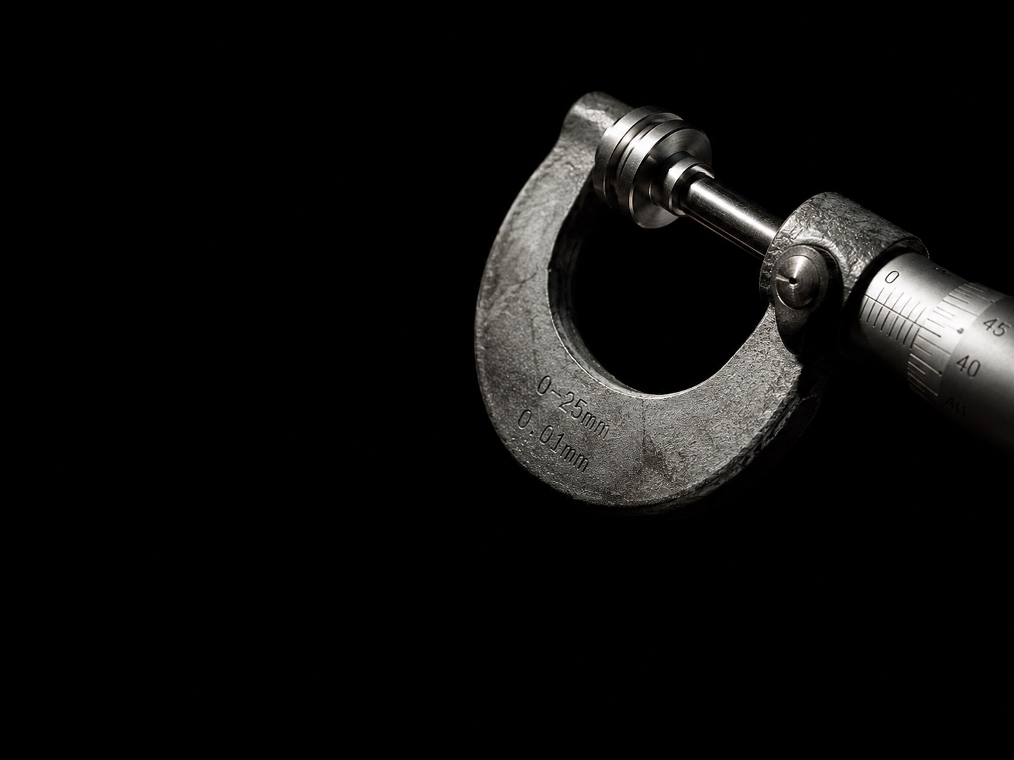 A steel micrometer measuring a machined part against darkness